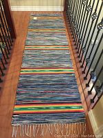 Full view of colorful Finnish rag rug stretched down a hallway with visible multicolored stripes and fringe on ends.