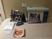 Full view of the holiday set laid out including the ceramic building, car, tree, bag of snow, documents, and box on a table surface under good lighting.