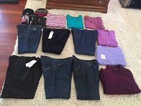 Full lot overview showing array of jeans, pants, tops, fleece jackets, and accessories laid out on carpet