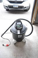 Shop-Vac Quiet Plus wet/dry vacuum unit with hose attached, unplugged, standing on garage floor with car in background.