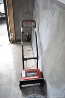 Full view of the snow thrower showing handle and front auger assembly indoors.