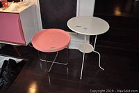 Pair of circular tables, one pink with chrome legs and one white with three-legged metal base, showing the top and sides.