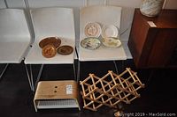 Seven decorative plates displayed on three white chairs; three wooden carved plates and four ceramic plates including an Asian design collectible.