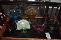 Seven vintage colored glass bowls displayed on wooden shelves, various styles and colors visible, showcasing the entire lot.