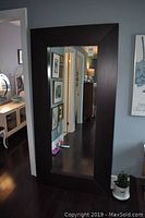 Full view of the mirror leaning against the wall, showing the dark wood frame and reflective glass in a room interior.