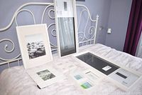 Eleven white picture frames of various sizes displayed on a white metal bedframe. Includes rectangular and square shapes, some with glass and placeholders inside.