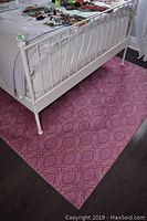 Pink synthetic geometric oval patterned rug under white metal bed frame on dark hardwood floor.