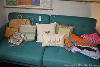 Full view of four bags, cushions, throw pillows, and blankets on teal sofa.