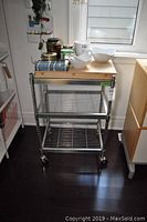 Front view of metal frame kitchen cart with butcher block top, wire mesh shelves below, and caster wheels.