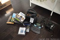 Full lot overview showing camcorder, audio recorder, alarm clock, label maker, and DVDs on wooden floor