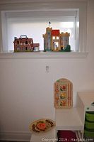 Photo showing vintage Fisher Price castle and Tudor style home toys on a windowsill with decorative plate below