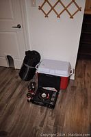Photo showing black sleeping bag, red and white cooler, four red propane lanterns, and portable butane stove.