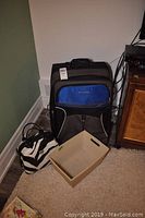 Columbia soft covered blue and black suitcase with front pocket, zebra print bag, and a beige storage box on floor next to wall