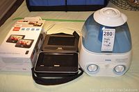 Two RCA mobile DVD systems in carrying cases with packaging box, next to a Vicks humidifier on a green surface.