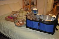 Wide shot of wire basket, large blue and black soft-sided bin containing metal pail and rolled wicker decor, placed on surface along with assorted wicker baskets.