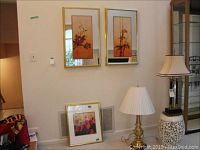 Photo of two Asian floral art prints framed with gold and mirror frames, both signed originals, hung on wall above other items.