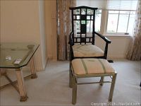 Full view of black lacquer Asian style chair with fabric seat and matching brass footstool with fabric top against living room background.
