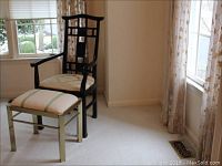 Photo showing full view of black lacquer Asian style chair with fabric covered seat, and brass footstool with fabric top placed on carpet near window.