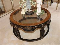 Front view of round coffee table showing glass top with painted Greek key design on the edge, and painted floral motif on black wood sides.