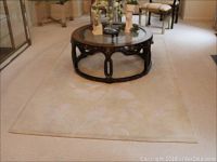 Full view of beige hand cut area rug with floral design and round coffee table on top.