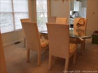 Set of six Parsons style dining chairs around a glass dining table, beige fabric upholstery, floral removable seat covers, seen from the dining room corner by window.
