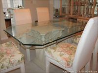 Dining table with clear thick glass top and six upholstered floral and cream chairs in a home dining room.