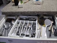Open flatware drawer showing Oneida stainless flatware with forks, spoons, knives, and serving spoons