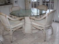 Overview of rattan pedestal dining table and four matching arm chairs with glass top in kitchen setting.