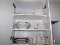 View of shelves inside cabinet showing stacked plates and cups with floral patterns.