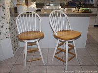 Front view of pair of wooden swivel counter stools with white spindle backs and natural wood seats in kitchen setting.