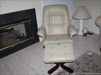 Full view of cream leather swivel chair with wooden legs and matching ottoman on tiled floor near fireplace and lamp.