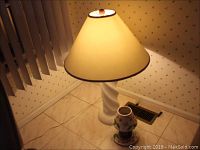 Full view of the ceramic table lamp with its beige fabric flared shade and additional candle plate set