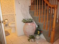Full view of the ceramic pot with faux ivy, floral wreath, and resin urn with twigs in hallway corner