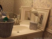 Photo showing two framed waterfowl prints, carved wooden bird on box stand, and wicker waste can placed on bathroom sink countertop
