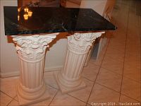Front view showing dark green marble top and two white detailed ceramic pedestal bases.