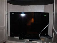 Front view of Sony Bravia TV mounted on stand inside cabinet, screen off, cables visible at back