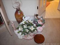 Photo of assorted faux floral arrangements, elephant figurine, brown glass vase with decorative twigs, small lighthouse, and other ceramic items.