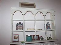 Front view of white wooden wall shelf with decorative items including two Princeton Gallery buildings, candle, fan, frame, lighthouses, mirror and ornament.