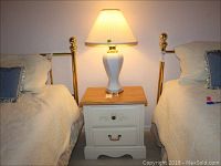 Overall view of the ceramic lamp positioned on the two-drawer nightstand between two beds.