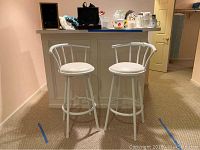 Two white bar stools with padded seats and vertical bar backrests, placed in front of a bar counter.