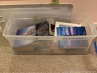Plastic bin partly filled with an assortment of nonfiction and fiction books visible through clear sides and on top.