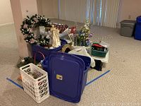 Wide view of assorted holiday decorations including wreath, angel figurine, baskets, and multiple storage bins with holiday items inside.