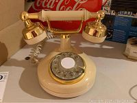 Vintage rotary dial telephone in off-white and brass colors with coiled cord and white handset