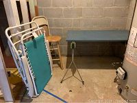 Photo showing work table, wood stool, metal folding chair, and outdoor lounge chair in basement setting.