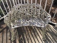 Overall view of white cast iron outdoor garden bench with curved backrest and seat featuring ornamental grapevine and floral patterns.