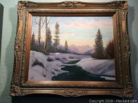Framed oil painting showing snowy mountains with a winding river and pine trees under a sunset sky.