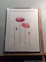 Framed watercolour art showing four flowers with long stems, two fully bloomed and two buds. Includes ruler for scale showing frame size approximately 24 by 18 inches.