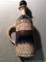 Side view of the pottery jug with stopper showing the glaze pattern and handle