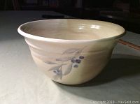 Side view showing hand-painted blue leaf and berries design on beige ceramic bowl