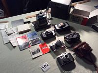 Four vintage cameras displayed on table with manuals, boxes, and original cases.